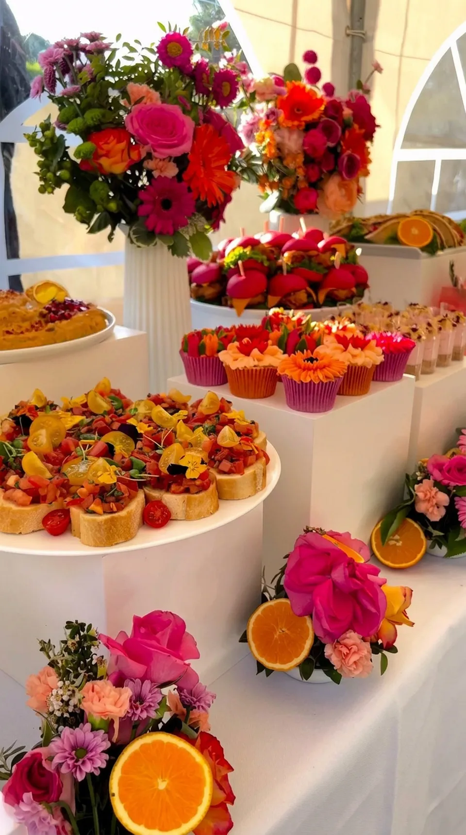 A colourful catered dessert table styled with flowers, cupcakes and fresh citrus